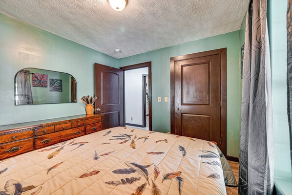 A bedroom with a bed, dresser, mirror, and a door leading to another room.