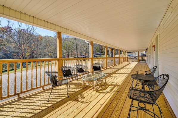 A covered porch with wooden railings, metal chairs, and a glass table. - Bonnieville Farmhouse on 69 Acres w/ Porch! (Bonnieville)