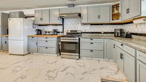 A modern kitchen with grey cabinets, a stainless steel refrigerator, a built-in oven, and a granite countertop. - Bonnieville Farmhouse on 69 Acres w/ Porch! (Bonnieville)