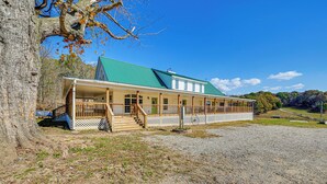 A two-story building with a green roof, a covered porch, and a gravel driveway. - Bonnieville Farmhouse on 69 Acres w/ Porch! (Bonnieville)