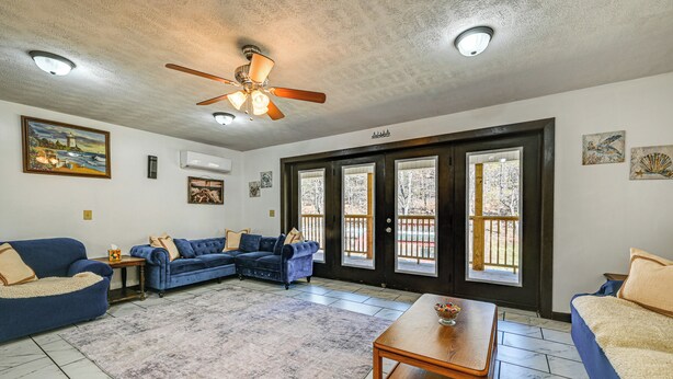 A living room with a blue sofa, a wooden coffee table, and a large window with a view of trees. - Bonnieville Farmhouse on 69 Acres w/ Porch! (Bonnieville)