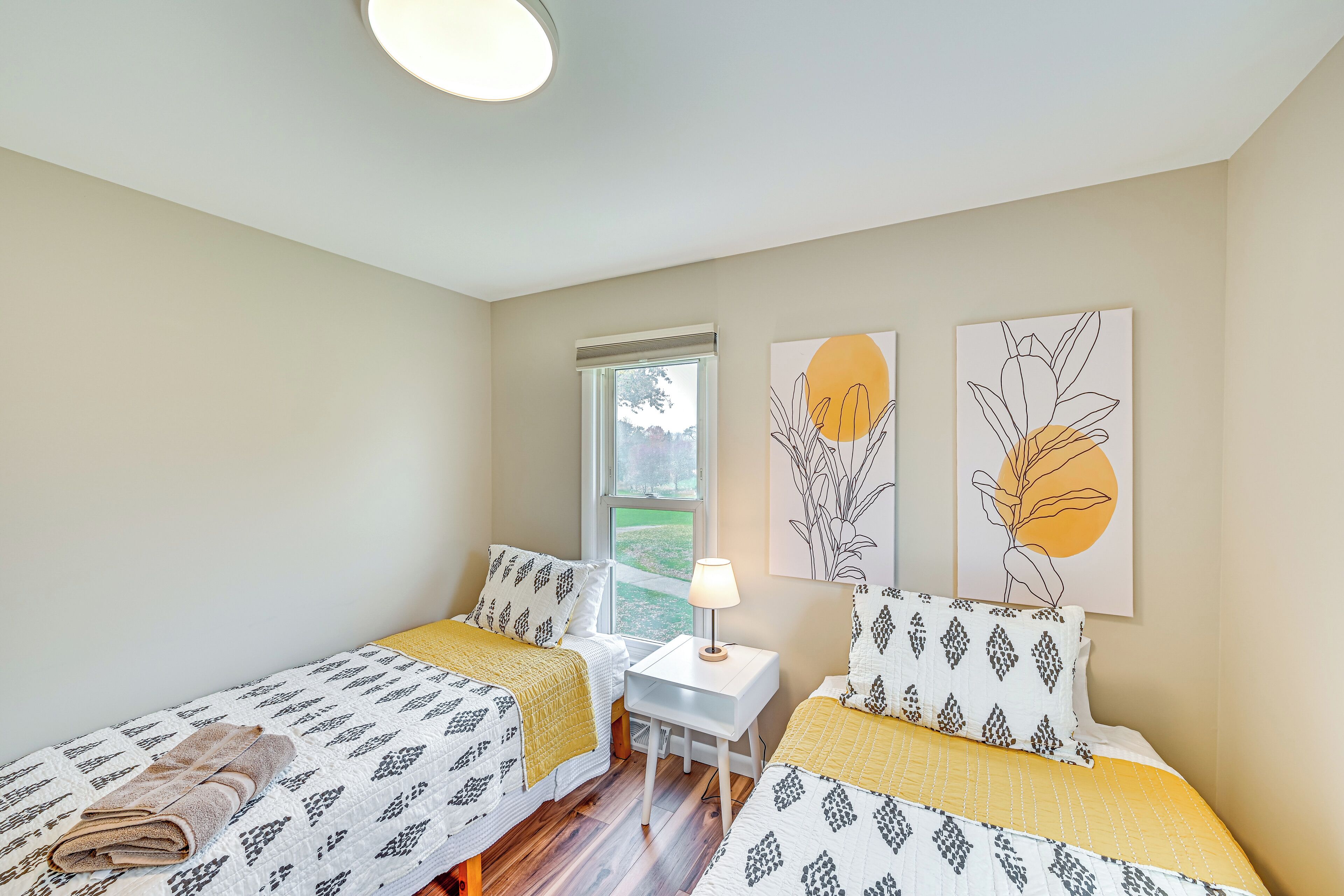 Une chambre avec deux lits, une petite table et des œuvres d’art accrochées aux murs.