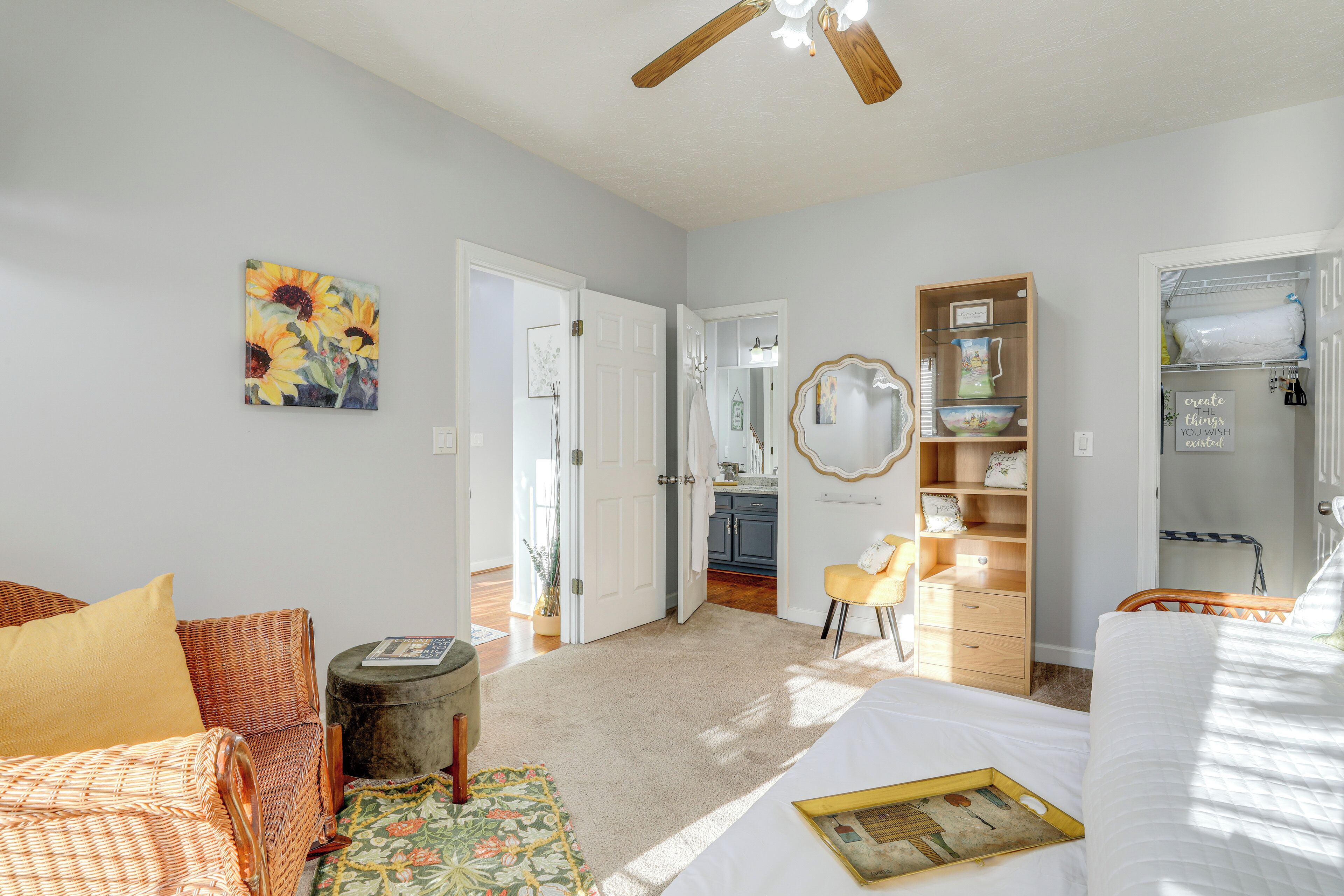 Une chambre à coucher comprenant un lit, une chaise, une petite table, une bibliothèque et une porte donnant sur une salle de bain.