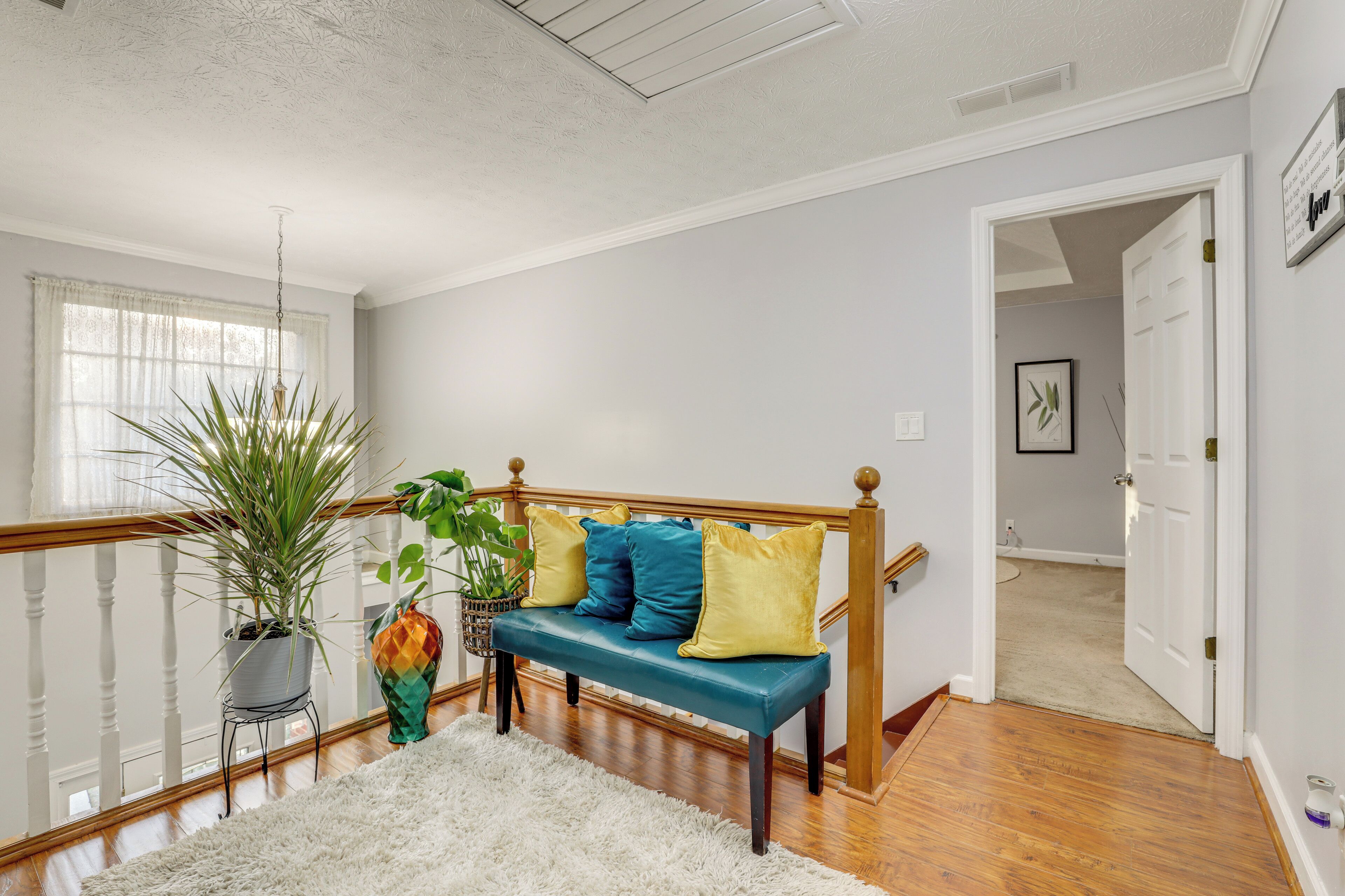 A staircase with a wooden handrail, a bench with cushions, a potted plant, and a white rug.