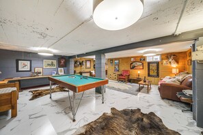 Ein Zimmer mit Billardtisch, Ledersofa und Kamin.
