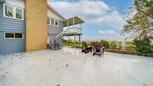 Ein Haus mit überdachter Terrasse, Sitzgelegenheiten im Freien und einer Treppe zu einer Außenterrasse.