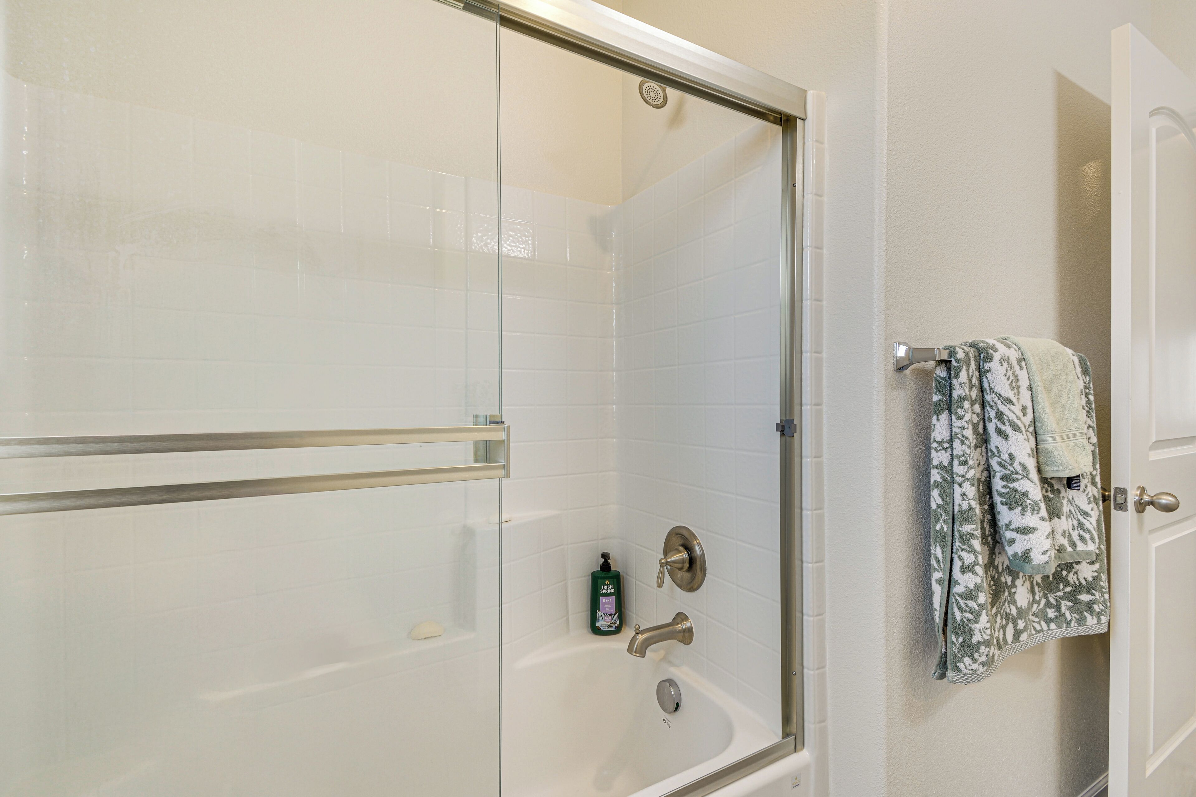 Una doccia con pareti in vetro, un maniglione metallico, una porta in vetro e un portasciugamani con asciugamani decorati.