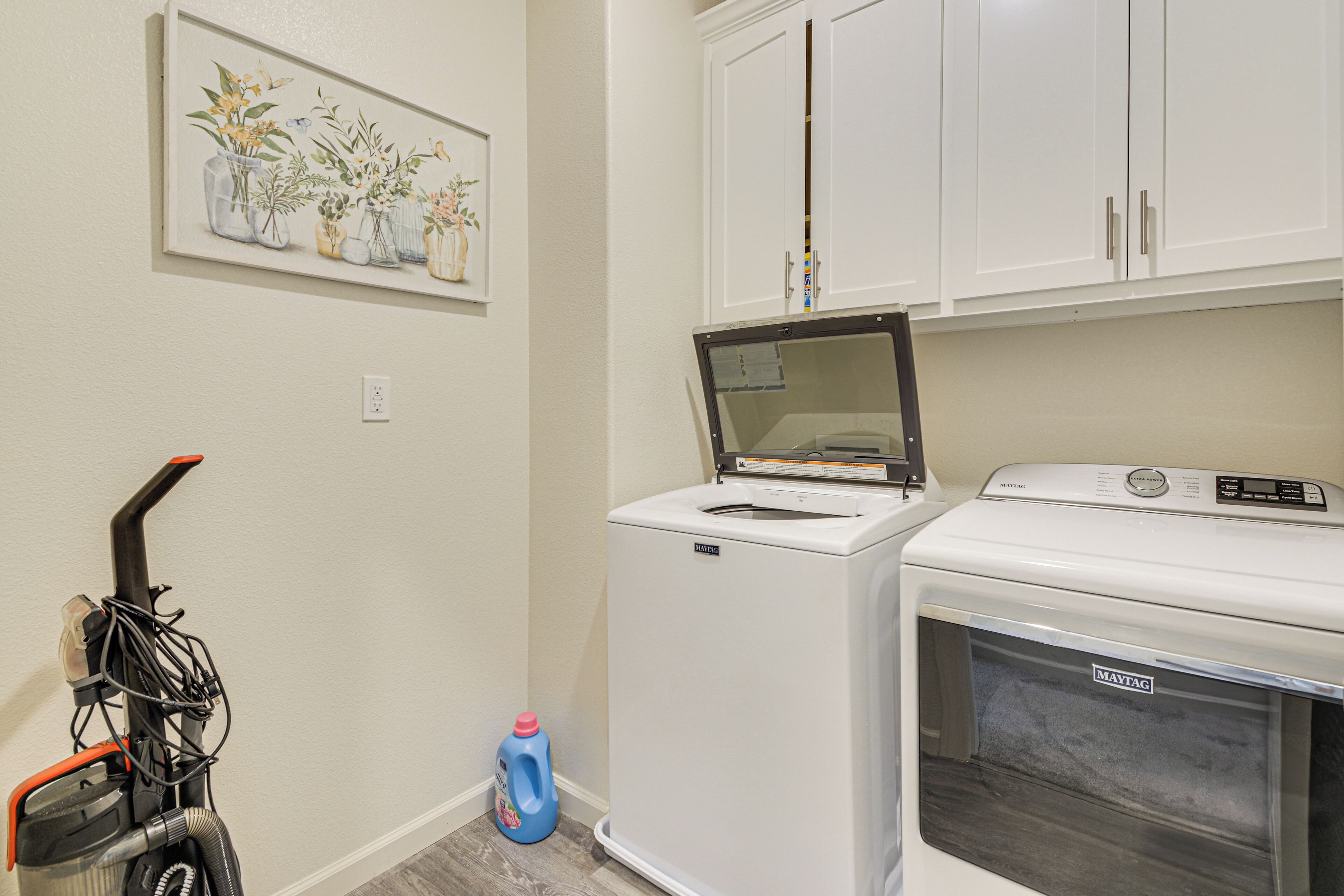 A laundry room with a washing machine, dryer, and a wall-mounted rack with a vacuum cleaner.