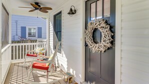 Une véranda avec des fauteuils à bascule blancs, un ventilateur de plafond et une guirlande décorative sur la porte.