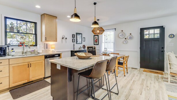 Une cuisine moderne avec des meubles en bois, un îlot central doté de tabourets de bar, un éclairage suspendu et une vue sur l’extérieur grâce à une grande fenêtre.