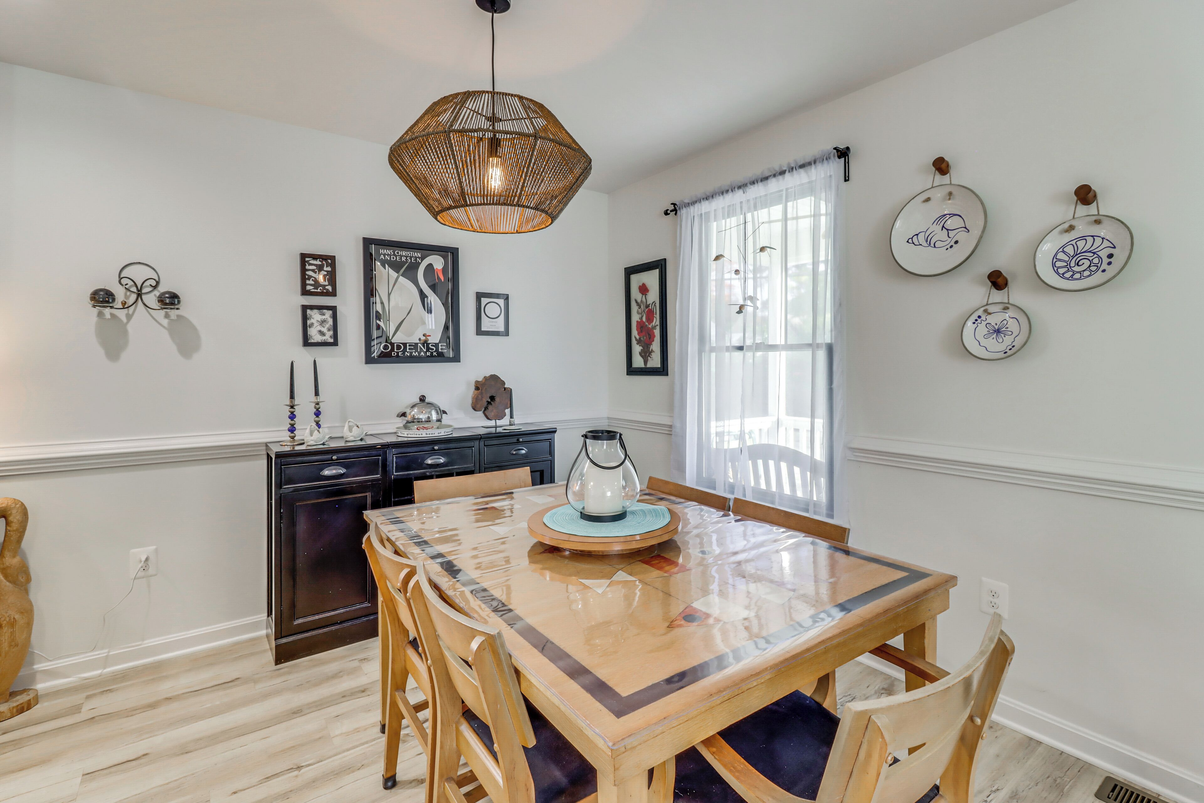 A dining area with a wooden table and chairs, a hanging light fixture, and wall-mounted plates.