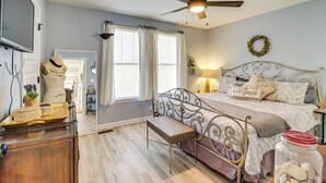 Une chambre à coucher comprenant un lit, un ventilateur de plafond, un banc, une commode et une fenêtre avec des rideaux.