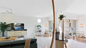 A modern living room with a sofa, coffee table, and a television. There are wicker chairs and a small table with a plant. - Stunning Resort Apartment with Gym and Pool Access (Westcourt)