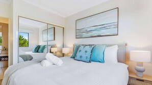 A well-lit bedroom with a large bed, two bedside lamps, a mirror, and a painting on the wall. - Stunning Resort Apartment with Gym and Pool Access (Westcourt)