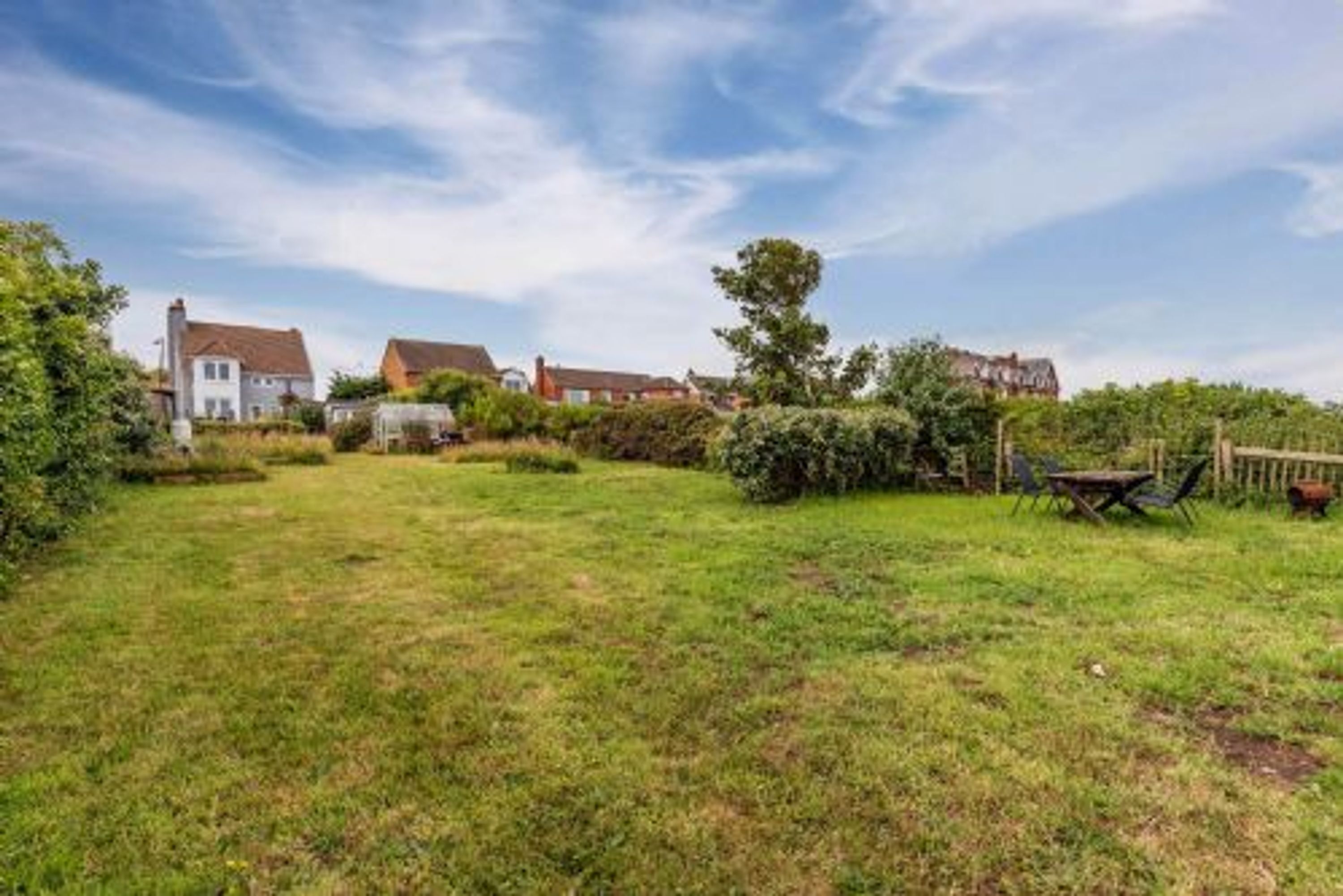 A grassy backyard with a wooden table and chairs, surrounded by houses.
