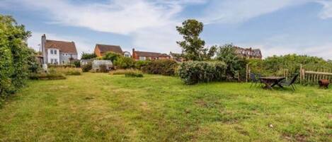 A grassy backyard with a wooden table and chairs, surrounded by houses.