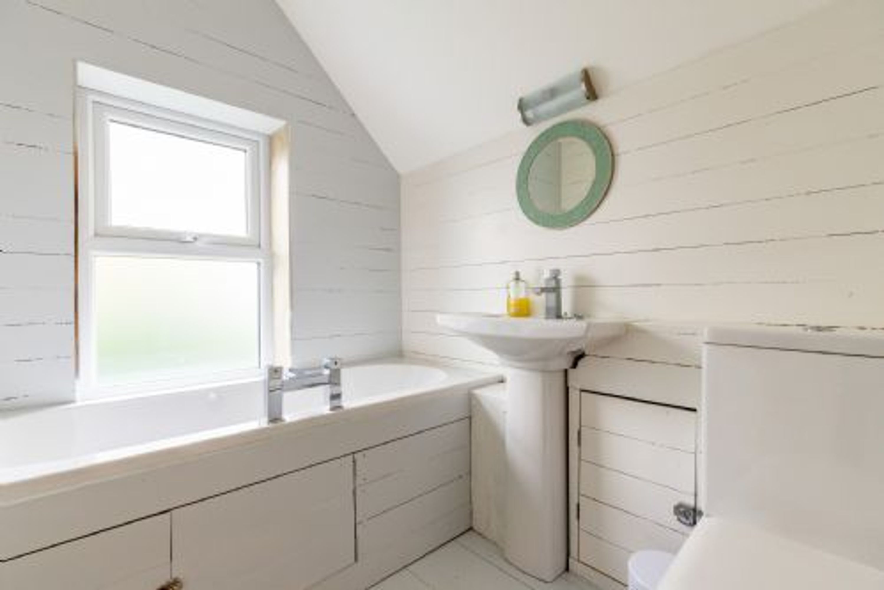 Un baño con ventana, lavamanos e inodoro.