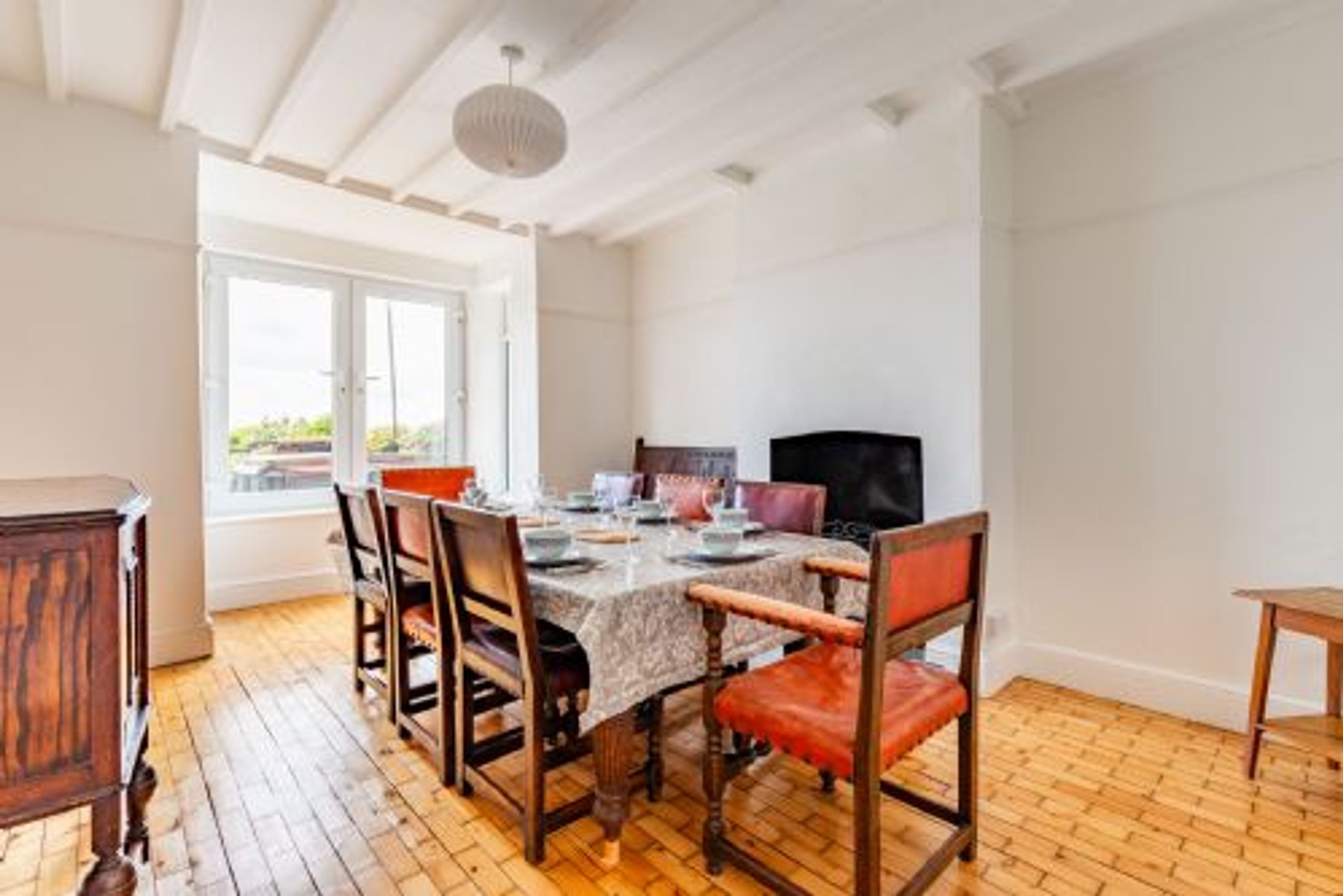 Un comedor con una mesa dispuesta para seis personas, sillas de madera y un televisor sobre un mueble.