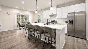 A modern kitchen with white cabinets, a stainless steel refrigerator, and a bar area with stools.