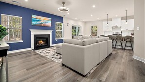 A modern living room with a fireplace, a large sofa, and a dining area with bar stools.