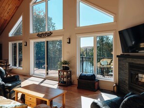 Amplia sala de estar con ventanas grandes, chimenea y televisor.