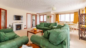 A spacious living room with green upholstered sofas, a flat-screen TV mounted on the wall, a fireplace, and a dining area with yellow curtains. - Host Stay Cransley (Great Yarmouth)