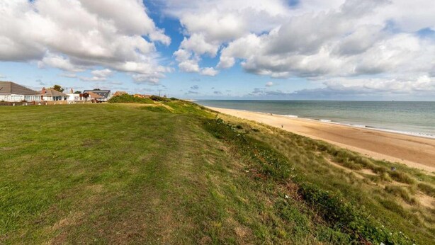 A coastal landscape with a grassy area, a sandy beach, and a row of houses in the background. - Host Stay Cransley (Great Yarmouth)