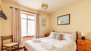 A neatly arranged bedroom with a bed, a chair, a nightstand, and a window with curtains. - Host Stay Cransley (Great Yarmouth)