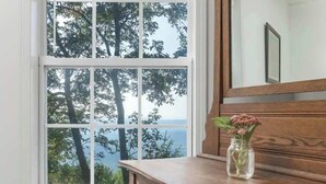 A room with a large window offering a view of trees and a body of water. A wooden dresser with a vase of flowers is visible. - The Brow House with Stunning Views! Sunsets (Lookout Mountain)