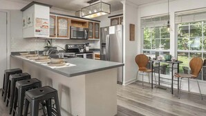 A modern kitchen with a central island, stainless steel appliances, and a dining area with two chairs and a table. - The Brow House with Stunning Views! Sunsets (Lookout Mountain)