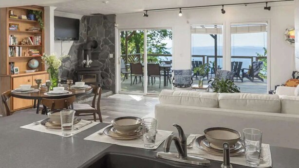 A modern kitchen with a stone backsplash, dining area with a table set for four, and a view of the outdoors. - The Brow House with Stunning Views! Sunsets (Lookout Mountain)