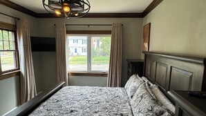 Et soveværelse med en stor seng, en træsenggavl, en loftsvifte og et vindue med gardiner.