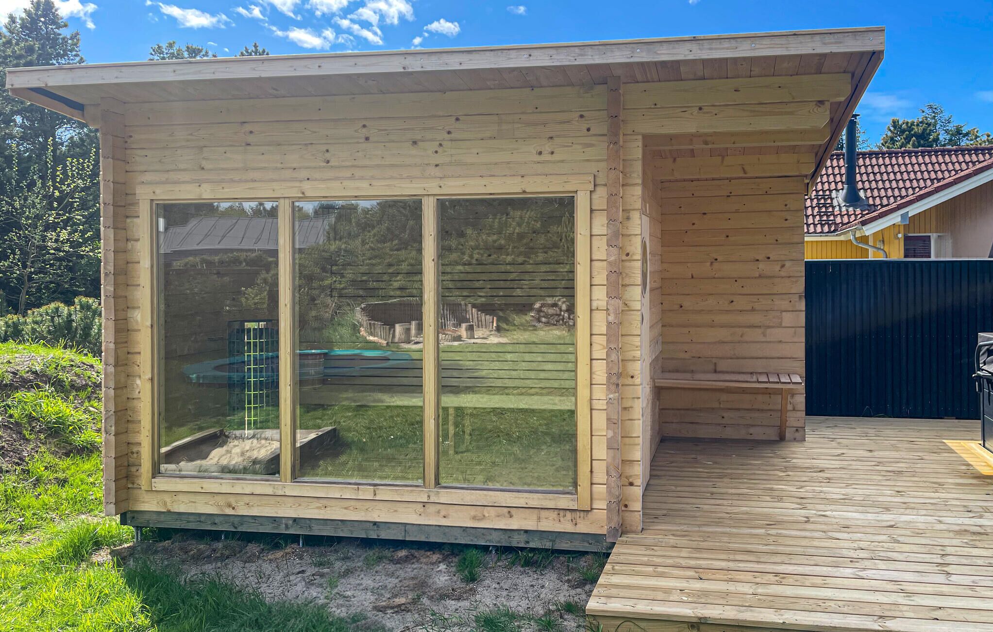 Una cabaña de madera con ventanas amplias, una terraza y vistas a un jardín con piscina.