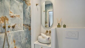 A bathroom with a marble shower wall, a round mirror, a white sink, and a wall-mounted heater. - Eiffel Tower Apartment Invalides (Paris)