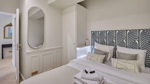 A hotel room with a large bed, a mirror, a decorative headboard, and a door leading to another room. - Eiffel Tower Apartment Invalides (Paris)