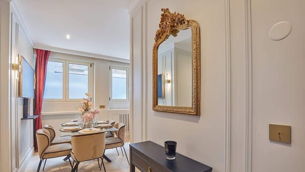 A dining area with a table set for four, a large ornate mirror on the wall, and a console table with a black vase. - Eiffel Tower Apartment Invalides (Paris)