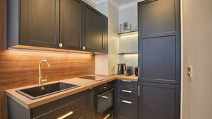 A modern kitchen with dark cabinetry, a wooden countertop, a sink, and a built-in oven. - Eiffel Tower Apartment Invalides (Paris)