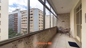 Un balcón con vistas a edificios altos, un muro de azulejos y un pequeño rincón de estar con sillas.