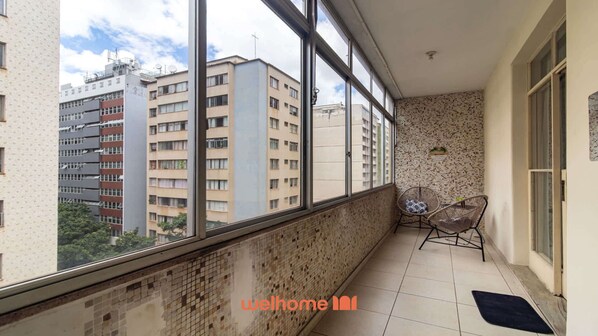A balcony with a view of high-rise buildings, a tiled wall, and a small seating area with chairs.