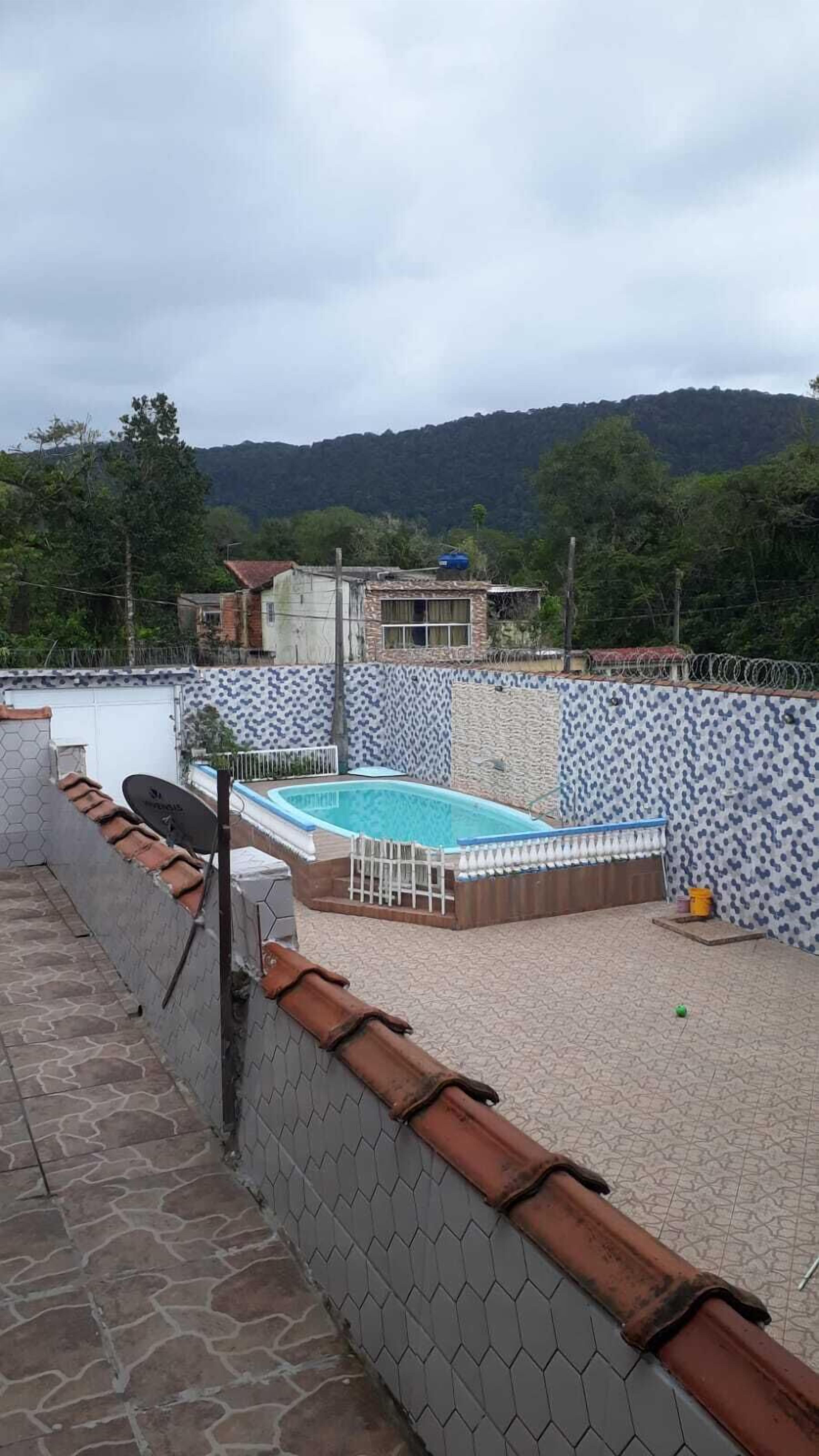 Uma piscina no terraço com piso hexagonal em mosaico, rodeada por um muro de tijolos baixo e uma cerca de metal.