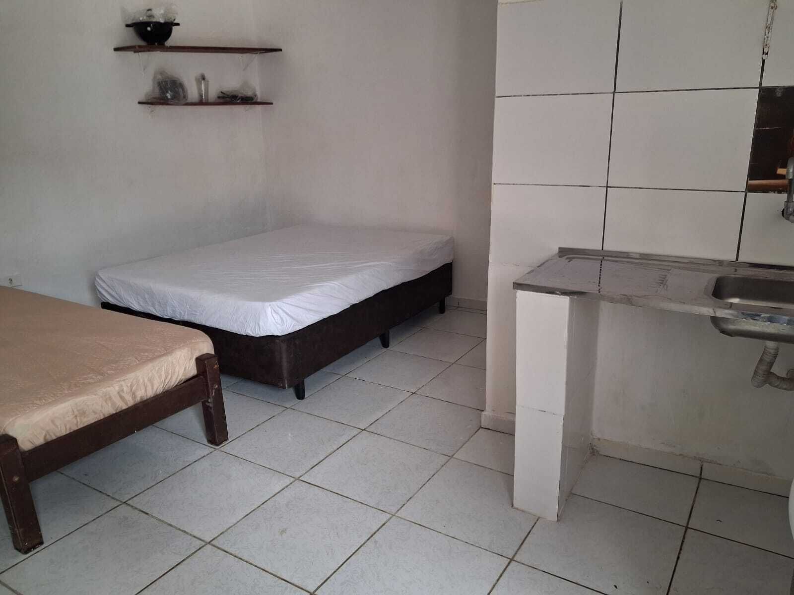 Ett litet, rent rum med en säng, en bänk, en hylla med toalettartiklar och ett handfat.