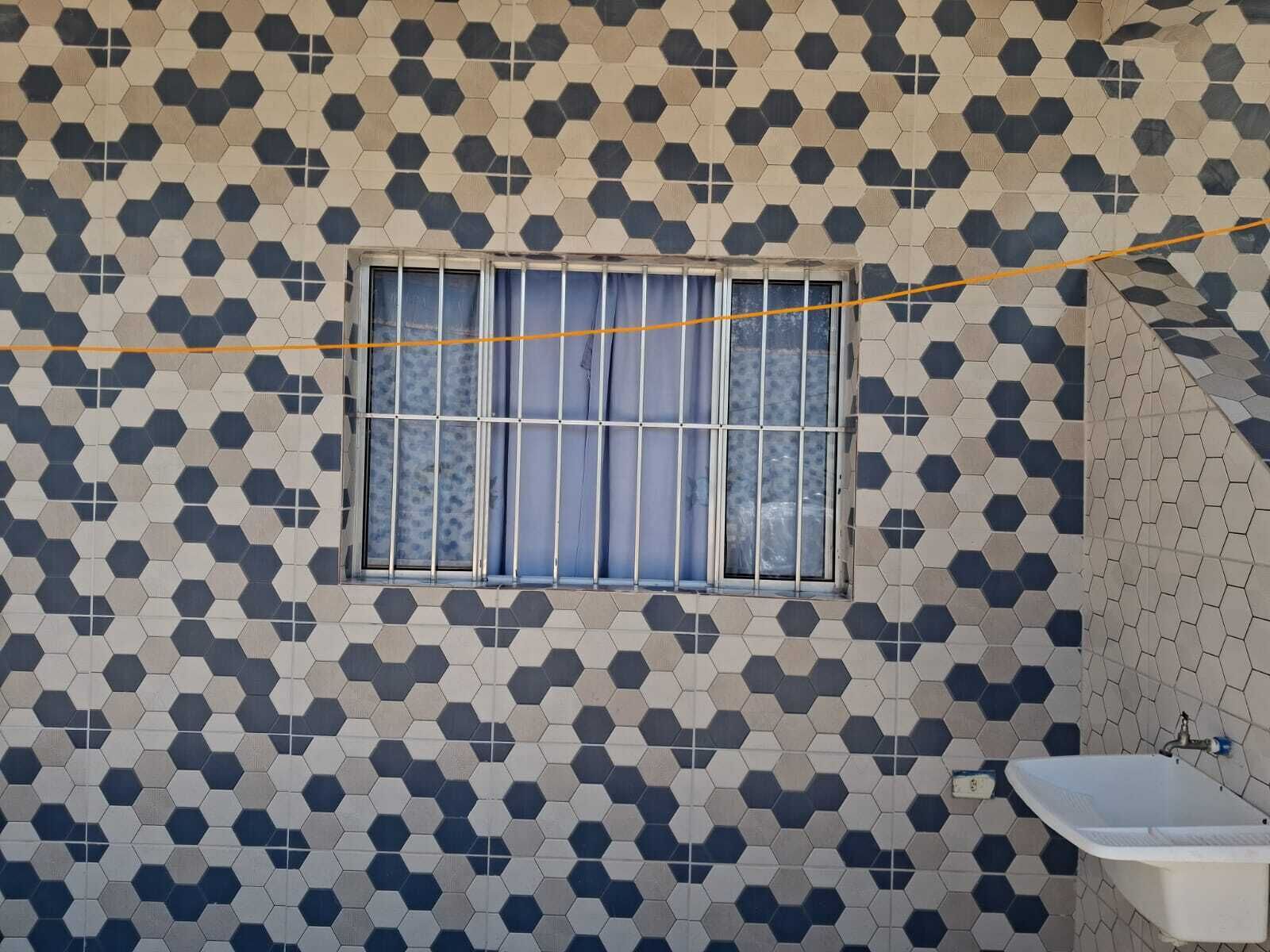 Un baño con un diseño geométrico de azulejos, una ventana con rejas y un lavabo blanco.
