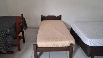 A small, single-bed room with a wooden bed frame, a matching wooden chair, and a small table with a checkered tablecloth.