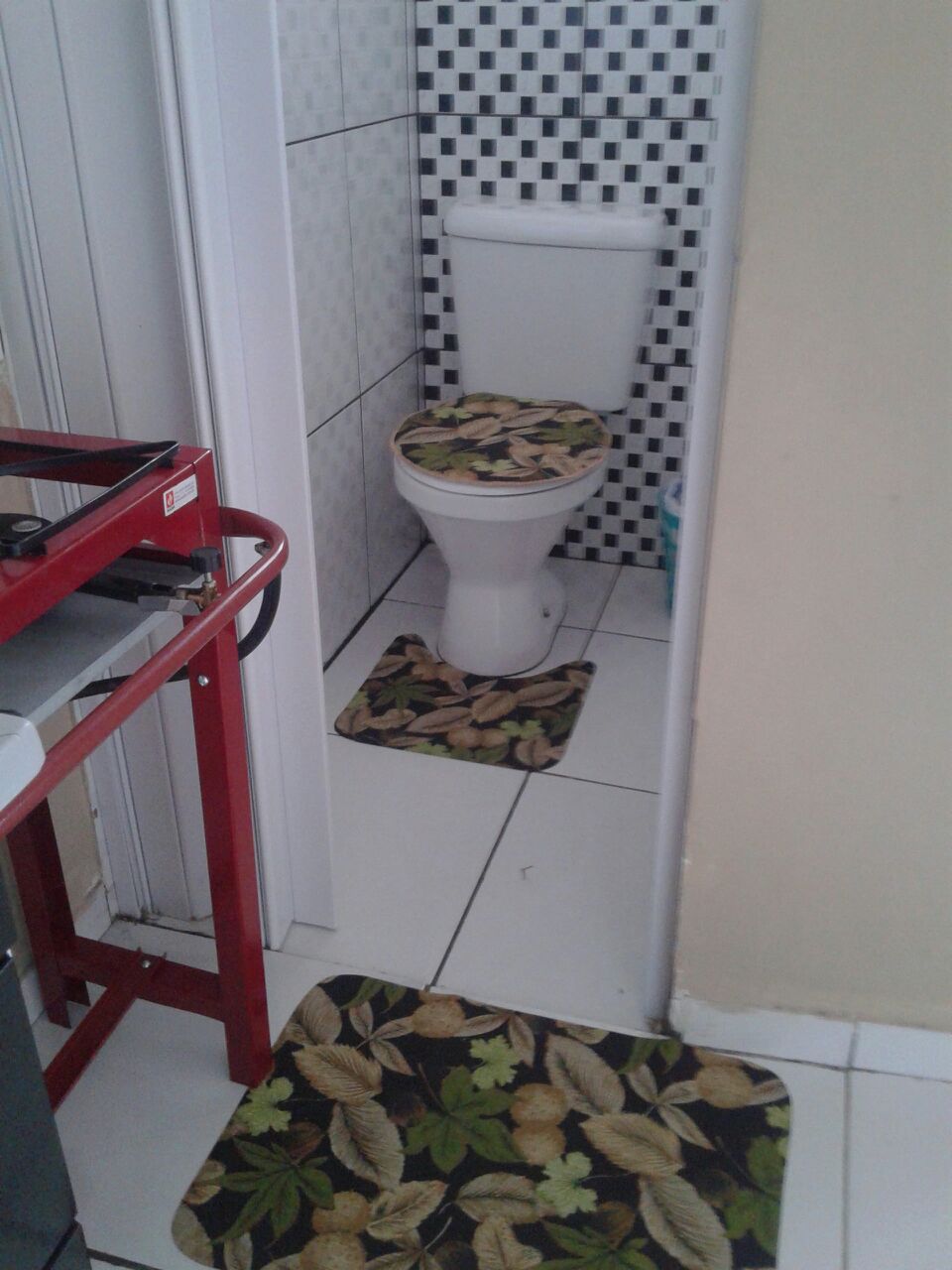 Et badeværelse med toilet, en rød metal skammel og en tæppe med mønster på gulvet.