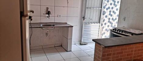 A kitchen with white tiles, a sink, a stove, and a window with a hexagonal pattern.