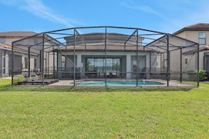 A covered outdoor pool area with a glass enclosure, a patio with outdoor furniture, and a lawn. - 209mcv - Balmoral Resort 4 Bedroom Home (Haines City)