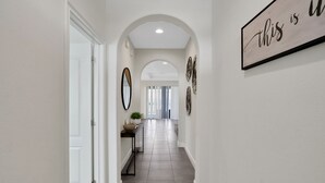 A hallway with a white door, a console table with a plant, and a sign on the wall. - 209mcv - Balmoral Resort 4 Bedroom Home (Haines City)