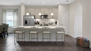 A modern kitchen with a central island, bar stools, stainless steel appliances, pendant lighting, and a dining area with chairs. - 209mcv - Balmoral Resort 4 Bedroom Home (Haines City)