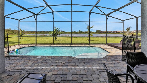 A covered outdoor area with a pool, patio furniture, and a view of a grassy field and distant buildings. - 209mcv - Balmoral Resort 4 Bedroom Home (Haines City)