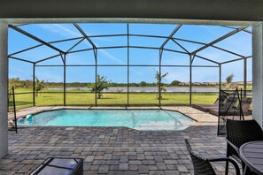 Un espacio al aire libre techado con piscina, mobiliario de patio y vistas a un campo de césped y edificios distantes.